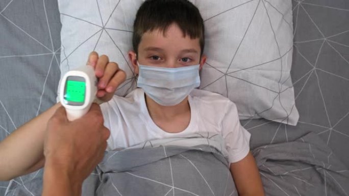 一个正常体温的康复男孩，显示在红外非接触式温度计的显示屏上，健康孩子的概念，母亲测量儿子的体温