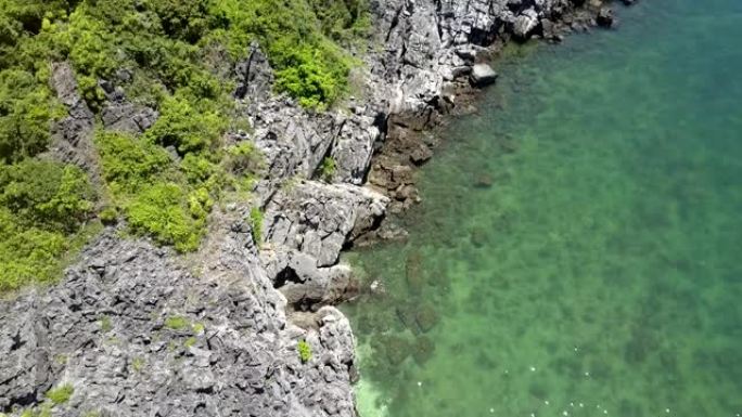 无人机沿着岩石海岸和蔚蓝的水之间的线飞行