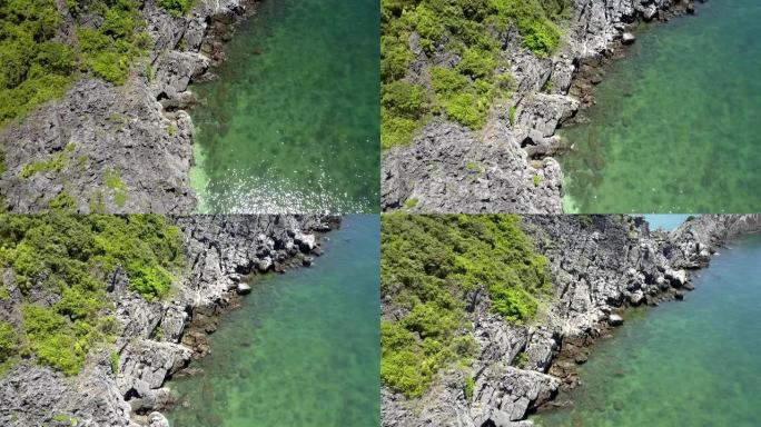 无人机沿着岩石海岸和蔚蓝的水之间的线飞行