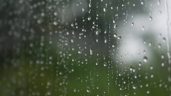 强烈的雨水冲向窗户玻璃并流下来。特写。雨季玻璃背景上的雨滴