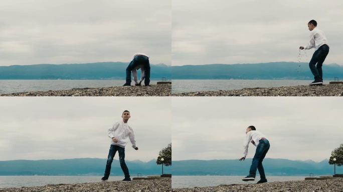 一个穿着白衬衫和牛仔裤的小男孩站在海滩上，向海浪投掷石块。慢动作