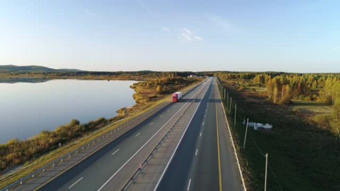 在农村地区繁忙的高速公路上行驶的红色半卡车和白色货运拖车的空中跟随镜头。阳光普照，天空蔚蓝。在幻影4