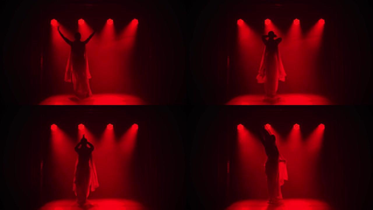 剪影一个穿着红色纱丽的年轻女孩舞者。印度民间舞蹈。在黑暗的工作室里拍摄，有烟雾和红色霓虹灯。慢动作