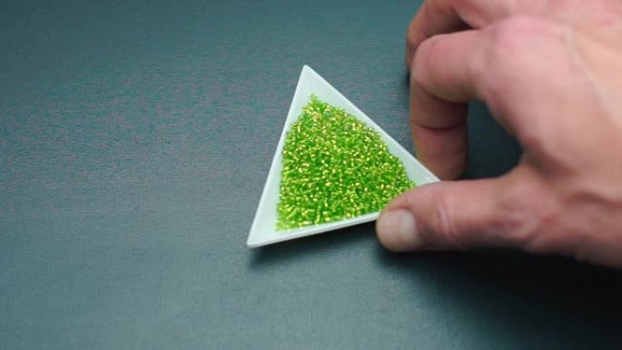 一只手的特写旋转一个带有绿色珠子的三角形盘子。