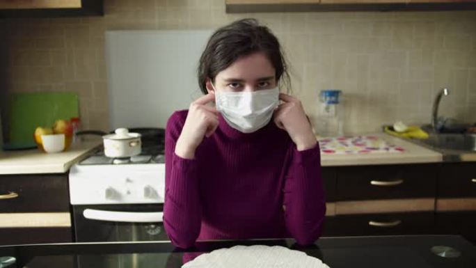 女孩坐在家里，在厨房的背景下取下医用口罩