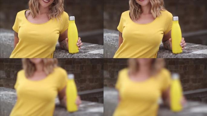 穿着黄色t恤的女性特写镜头，拿着黄色可重复使用的钢瓶