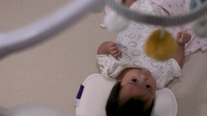 4k亚洲黑发婴儿婴儿躺在家里，用粉红色的毯子躺着，相机通过塑料天花板移动悬挂，头顶拍摄，卧室，儿童保
