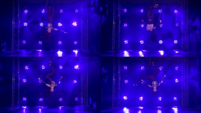 女空中飞人表演杂技元素，并在蓝色霓虹灯的背景下悬挂空中箍旋转。慢动作