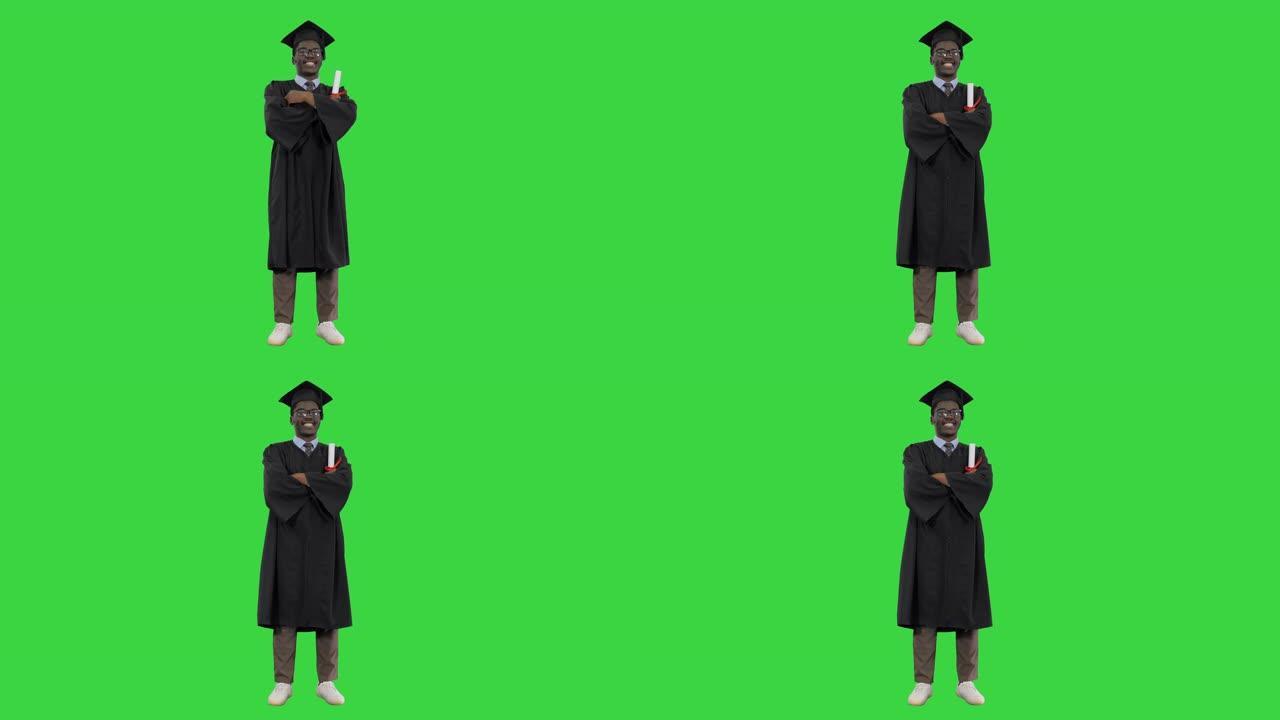 毕业长袍折叠双臂的非裔美国男学生在绿色屏幕上对着相机露出灿烂的笑容，色度键