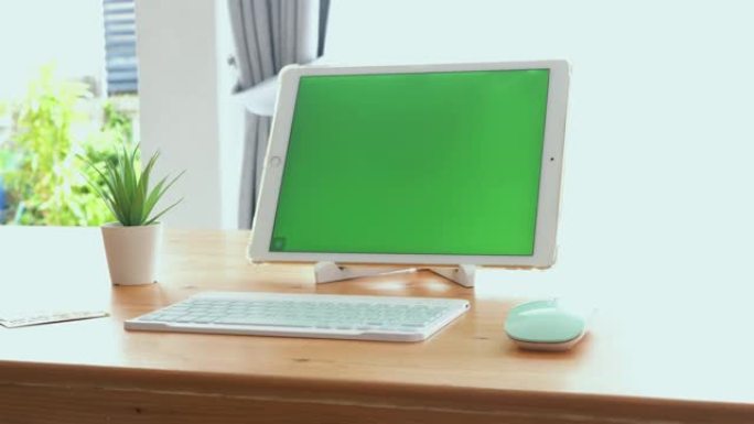 绿色屏幕数字平板电脑放在桌子上，家里有键盘和鼠标，工作工具概念。
