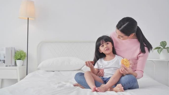 幸福的家庭母女俩在家床上吃甜甜圈。