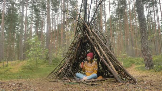 女人在松木间的小屋中喝热水瓶中的饮料