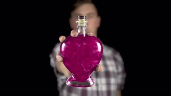 一个年轻人在相机里拿出一个装有爱情药水的瓶子。带有粉红色液体的心脏形式的玻璃瓶。情人节是所有恋人的日