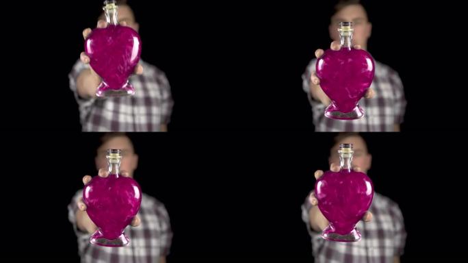 一个年轻人在相机里拿出一个装有爱情药水的瓶子。带有粉红色液体的心脏形式的玻璃瓶。情人节是所有恋人的日