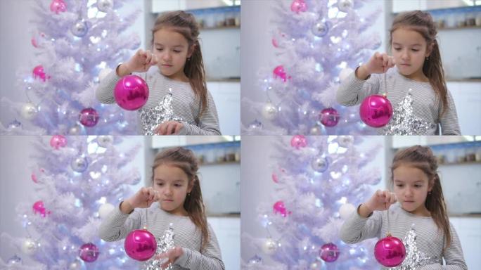 高兴可爱的孩子玩粉红色的摆设，左右摇摆，站在圣诞树旁，微笑着。