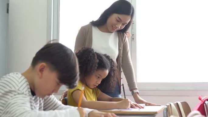 亚洲学校老师在课堂上协助学生。在学校工作的年轻女子帮助男孩写作，教育，支持，照顾