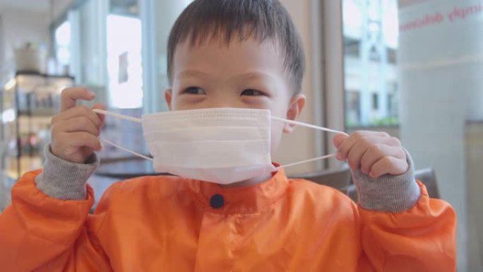亚洲3-4岁蹒跚学步男孩儿童佩戴/戴上防护医用口罩，防止细菌和病毒