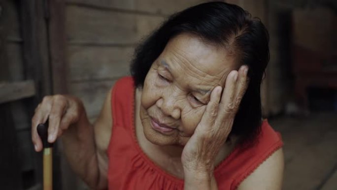 泰国老年妇女穿着圆领无袖衣领，头痛，担心在木制房屋中压力过大的脸
