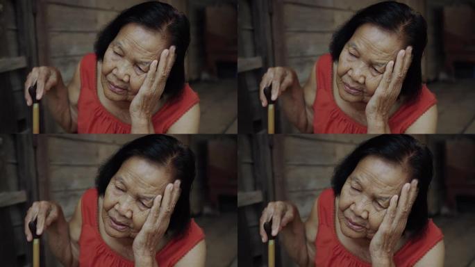 泰国老年妇女穿着圆领无袖衣领，头痛，担心在木制房屋中压力过大的脸