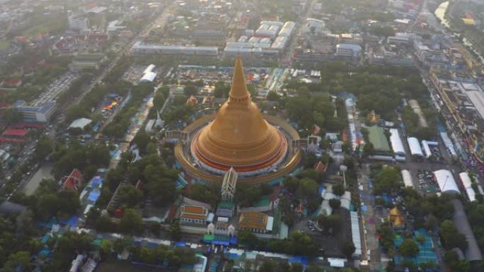 日落时Phra Pathommachedi寺的空中俯视图。带有民居的金色佛教宝塔，泰国纳康帕通区城市