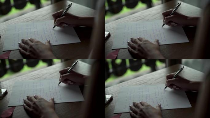 年轻女子用笔在白纸上写给她心爱的新郎的情书，坐在阳台附近房间的桌子上。手机和小麦花束就在附近。婚礼准