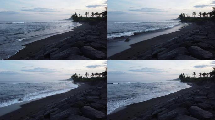 印度尼西亚巴厘岛Gianyar黑沙滩 (Pantai Saba) 日落的4k镜头。流云，蓝天，大黑石