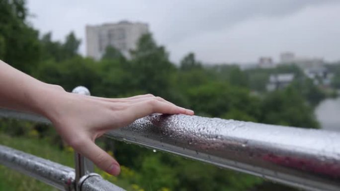 女性的手从防护装置的金属扶手上甩掉雨滴。