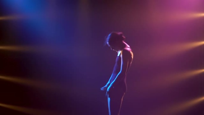 穿着黑色紧身衣的专业芭蕾舞演员优雅地跳舞芭蕾舞。在舞台上的动态聚光灯和烟雾中拍摄。美丽苗条身材的轮廓