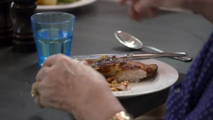 一名老年妇女用刀叉吃烤鸡晚餐