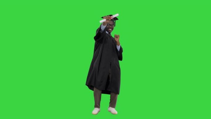兴奋的非裔美国男学生穿着毕业长袍，放弃了文凭，并在绿色屏幕上摆姿势，色度键