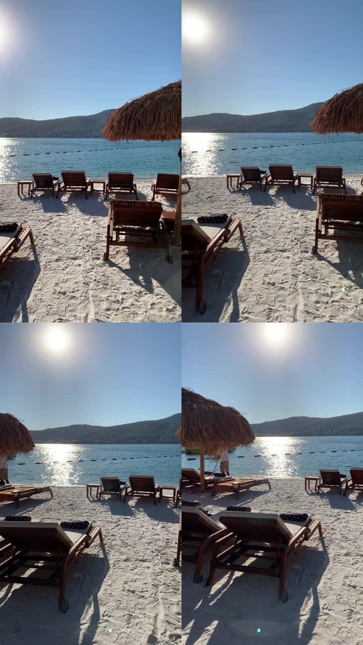 土耳其Lujo豪华酒店的4k翡翠泻湖在白色海滩上俯瞰常绿山丘，雪白的生态游艇，日光浴躺椅和竹伞
