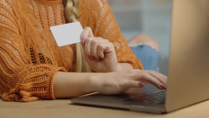 一名年轻女子的手拿着一张信用卡，并在网上购买
