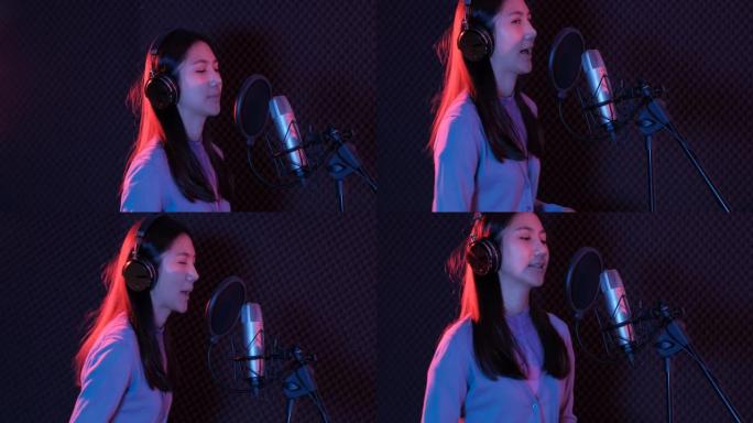 中镜头的年轻亚洲女性流行歌手在耳机中看着智能手机屏幕上的歌词，同时在麦克风中唱歌站在音乐录音棚的展位