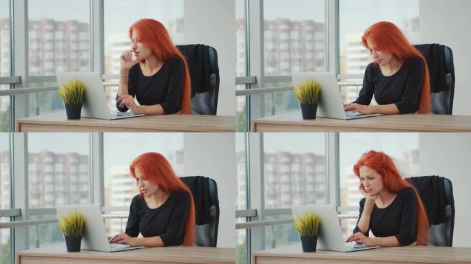 白人外表和红头发的年轻迷人女人在办公室用笔记本电脑工作。女人屏住呼吸，思考和工作。