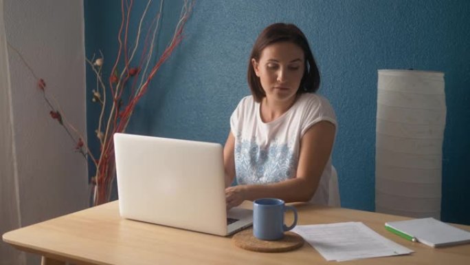 年轻快乐的女人坐在明亮的公寓或办公室内部，在笔记本电脑上工作，自由职业者女孩在工作，远程学习的概念学