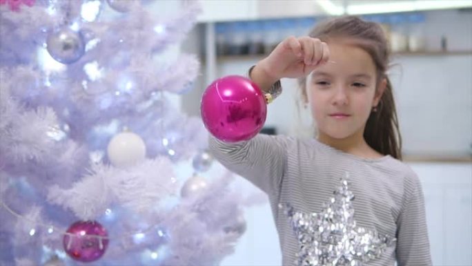 高兴可爱的孩子玩粉红色的摆设，左右摇摆，站在圣诞树旁，微笑着。