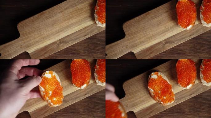 一个人的手将带有红色鱼子酱的三明治放在木板上。