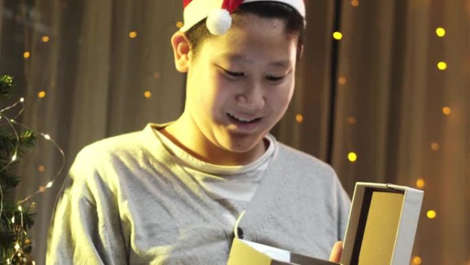 亚洲男孩戴着圣诞老人的帽子，在家里用惊喜打开圣诞礼盒。