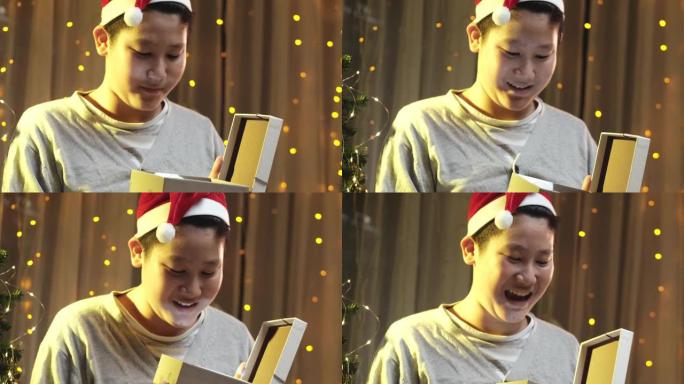 亚洲男孩戴着圣诞老人的帽子，在家里用惊喜打开圣诞礼盒。