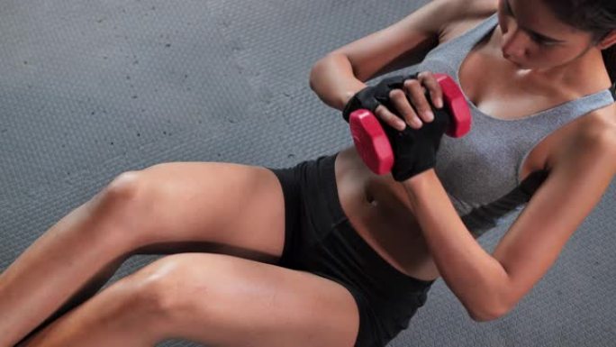 亚洲少女执行腹部肌肉在健身房使用哑铃，在健身房锻炼。