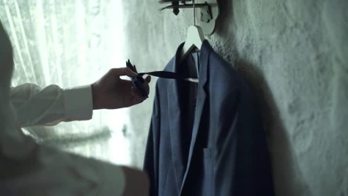 奥地利Kuchl - 2019年8月23日:新郎的早晨准备。男士的夹克和领结挂在木衣架上。新郎拿领结