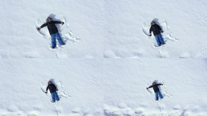 快乐的男孩躺在闪闪发光的雪地上，挥舞着他的胳膊和腿，使雪天使的鸟瞰图滑动。孩子穿着暖和的冬装在雪地里