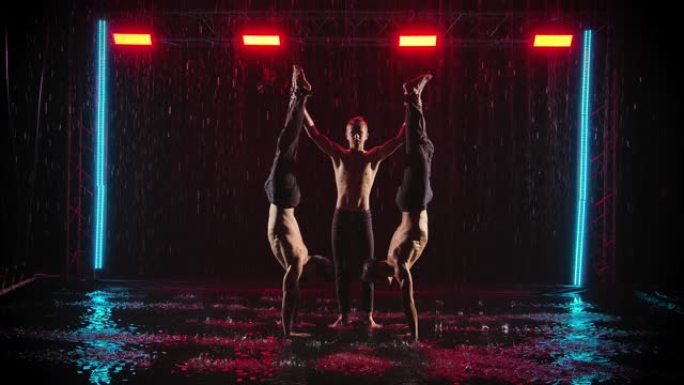 男人在雨中表演杂技特技。三位男杂技演员的专业表演。黑色背景，红色霓虹灯。慢动作