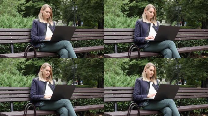 年轻迷人的女人坐在公园的长凳上，使用笔记本电脑