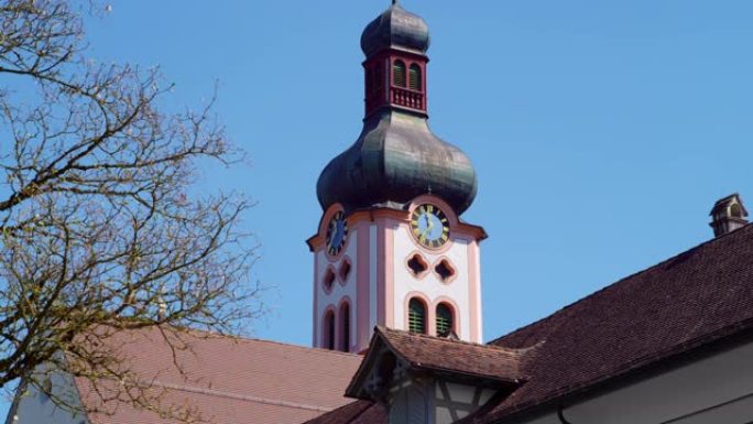 美丽的巴洛克和洛可可风格的古色古香的粉红色教堂塔，棕色的红砖屋顶，前面是没有云彩的蓝天，蓝色表盘的时