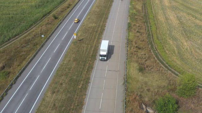 载货拖车在空旷的道路上行驶并运输货物的卡车的鸟瞰图。飞越送货卡车，沿着乡村的高速公路行驶。周围美丽的