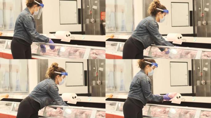 成熟的女人在超市过道上购买肉类，戴着防护口罩，手术手套和面罩