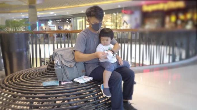 亚洲父亲与儿子坐在商场时戴着保护性口罩使用洗手液凝胶
