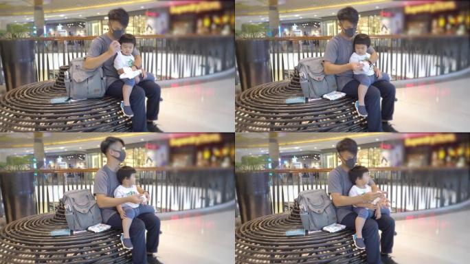 亚洲父亲与儿子坐在商场时戴着保护性口罩使用洗手液凝胶