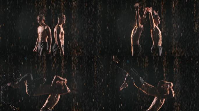 两名体操杂技演员在雨中保持平衡。强壮的运动员在团队合作中表演困难的技巧。在黑色背景上拍摄，慢动作照明
